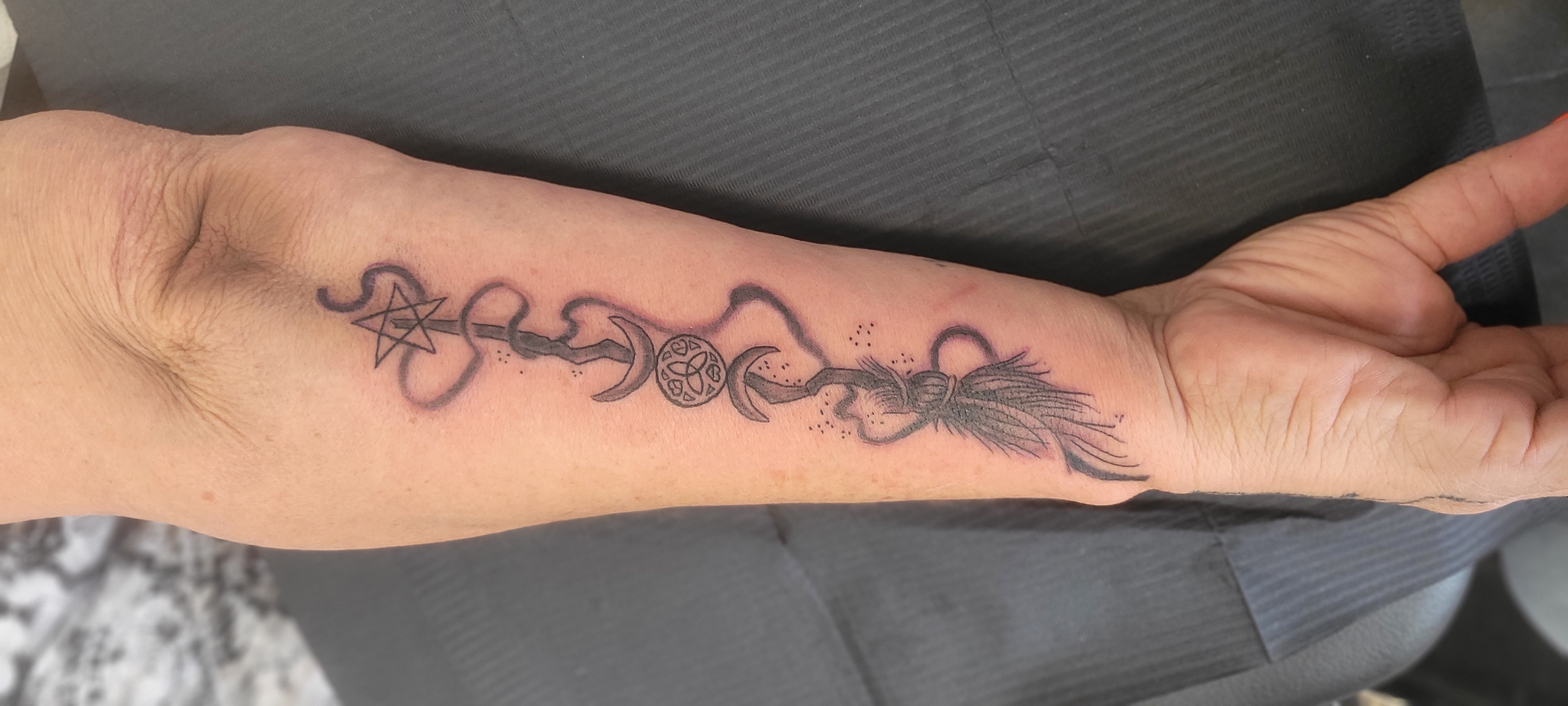 Tattoo von einem Besen mit Symbolen auf Unterarm